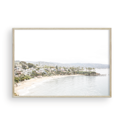 Horizontal coastal photography featuring a beach scene with a calm ocean and beach homes lining the shoreline, located in Laguna California. Photograph in minimalist mock up.