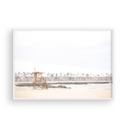 Landscape beach photography of Newport Beach, featuring lifeguard tower 56 on the sand with ocean waves and coastal houses in the background. A great Newport Beach photography print. Photograph in minimalist mock up