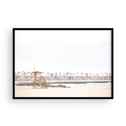 Landscape beach photography of Newport Beach, featuring lifeguard tower 56 on the sand with ocean waves and coastal houses in the background. A great Newport Beach photography print. Photograph in minimalist mock up