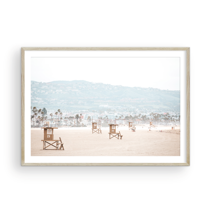 Landscape beach photography of Santa Monica State Beach with multiple lifeguard towers on the vast sandy expanse and hazy hills in the background. Photograph in minimalist mock up