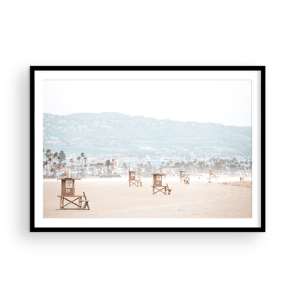 Landscape beach photography of Santa Monica State Beach with multiple lifeguard towers on the vast sandy expanse and hazy hills in the background. Photograph in minimalist mock up
