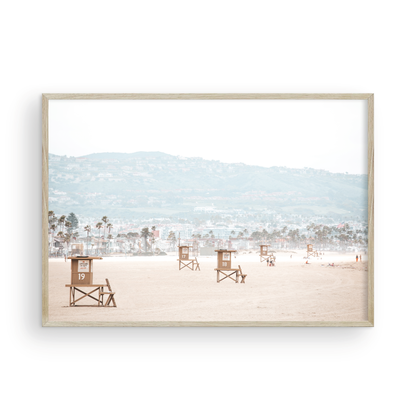 Landscape beach photography of Santa Monica State Beach with multiple lifeguard towers on the vast sandy expanse and hazy hills in the background. Photograph in minimalist mock up
