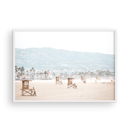 Landscape beach photography of Santa Monica State Beach with multiple lifeguard towers on the vast sandy expanse and hazy hills in the background. Photograph in minimalist mock up