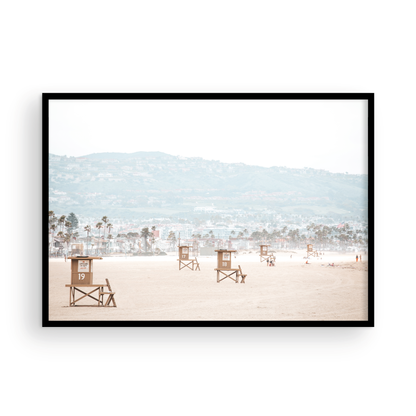Landscape beach photography of Santa Monica State Beach with multiple lifeguard towers on the vast sandy expanse and hazy hills in the background. Photograph in minimalist mock up