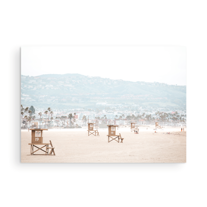 Landscape beach photography of Santa Monica State Beach with multiple lifeguard towers on the vast sandy expanse and hazy hills in the background. Photograph in minimalist mock up