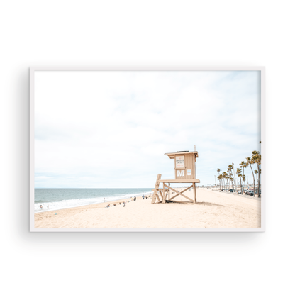 A wide landscape coastal photography view of Newport Beach in Southern California, featuring a row of tall palm trees, a lifeguard tower, and people enjoying the calm beach. Photograph in minimalist mock up.