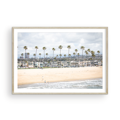 Landscape beach photography of Newport Beach, California, showing a wide sandy beach, a long line of tall palm trees, and coastal homes. Photograph in minimalist mock up.