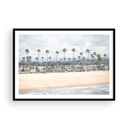 Landscape beach photography of Newport Beach, California, showing a wide sandy beach, a long line of tall palm trees, and coastal homes. Photograph in minimalist mock up.