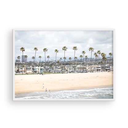 Landscape beach photography of Newport Beach, California, showing a wide sandy beach, a long line of tall palm trees, and coastal homes. Photograph in minimalist mock up.