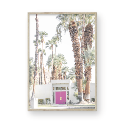 Vertical tropical print featuring a Palm Springs residence with a vibrant pink door, framed by numerous tall palm trees. This image is a fun beach photography style print. Photograph in minimalist mock up.