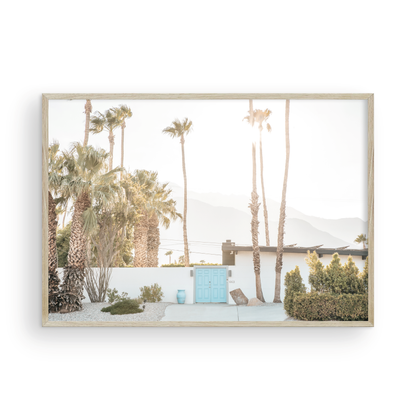 Coastal print of a Palm Springs home with a bright blue door, surrounded by tall palm trees and distant mountains, embodying summer vibes wall art. Photograph in minimalist mock up.
