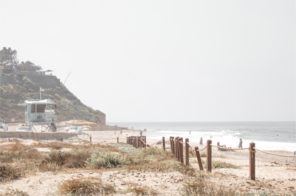 Landscape coastal photography of a light-colored lifeguard tower at a Southern California beach, with a rustic wooden fence leading towards the ocean waves. This tranquil beachscape print is ideal for beach cottage wall decor or a calm beach print. 