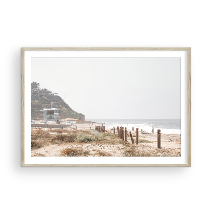 Landscape coastal photography of a light-colored lifeguard tower at a Southern California beach, with a rustic wooden fence leading towards the ocean waves. This tranquil beachscape print is ideal for beach cottage wall decor or a calm beach print. Photograph in minimalist mock up.