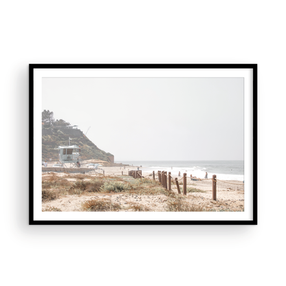 Landscape coastal photography of a light-colored lifeguard tower at a Southern California beach, with a rustic wooden fence leading towards the ocean waves. This tranquil beachscape print is ideal for beach cottage wall decor or a calm beach print. Photograph in minimalist mock up.