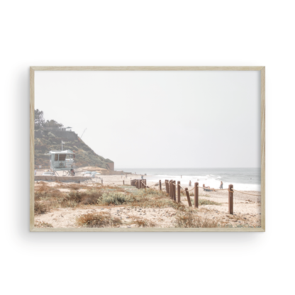 Landscape coastal photography of a light-colored lifeguard tower at a Southern California beach, with a rustic wooden fence leading towards the ocean waves. This tranquil beachscape print is ideal for beach cottage wall decor or a calm beach print. Photograph in minimalist mock up.
