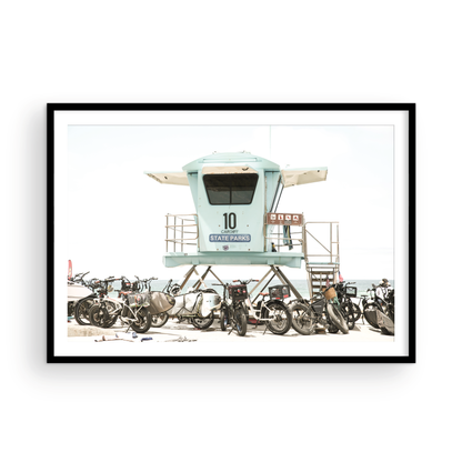 Captured in a horizontal San Diego print, a light blue Lifeguard Tower (number 10) stands prominently among numerous bicycles are parked nearby. Located in Seaside Beach, San Diego, California. Photograph in minimalist mock up.