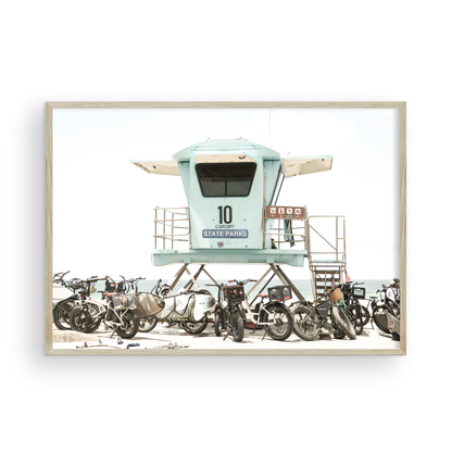 Captured in a horizontal San Diego print, a light blue Lifeguard Tower (number 10) stands prominently among numerous bicycles are parked nearby. Located in Seaside Beach, San Diego, California. Photograph in minimalist mock up.