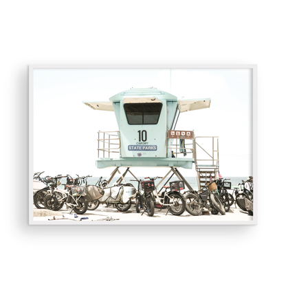 Captured in a horizontal San Diego print, a light blue Lifeguard Tower (number 10) stands prominently among numerous bicycles are parked nearby. Located in Seaside Beach, San Diego, California. Photograph in minimalist mock up.