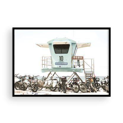 Captured in a horizontal San Diego print, a light blue Lifeguard Tower (number 10) stands prominently among numerous bicycles are parked nearby. Located in Seaside Beach, San Diego, California. Photograph in minimalist mock up.