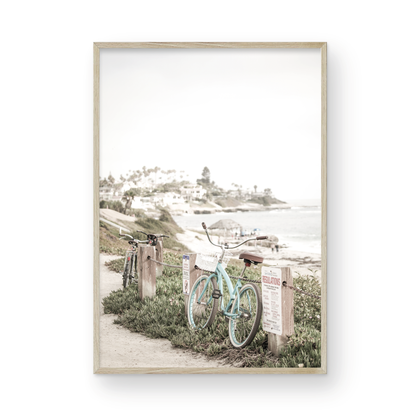 Fine art of horizontal landscape print by Southern California photographer Kim Dybczak of Salt Creek Prints, the image shows a light blue pastel beach cruiser leaning against a wooden post and chain fence. Another bicycle is visible behind it. The beach is in the background with people and a beach hut, located in Windansea Beach in La Jolla, California. Photograph in framed minimalist mock up
