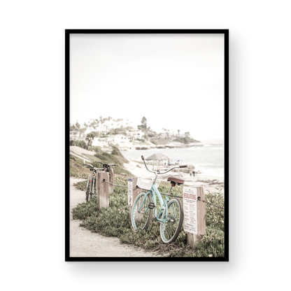 Fine art of horizontal landscape print by Southern California photographer Kim Dybczak of Salt Creek Prints, the image shows a light blue pastel beach cruiser leaning against a wooden post and chain fence. Another bicycle is visible behind it. The beach is in the background with people and a beach hut, located in Windansea Beach in La Jolla, California. Photograph in framed minimalist mock up