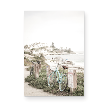 Fine art of horizontal landscape print by Southern California photographer Kim Dybczak of Salt Creek Prints, the image shows a light blue pastel beach cruiser leaning against a wooden post and chain fence. Another bicycle is visible behind it. The beach is in the background with people and a beach hut, located in Windansea Beach in La Jolla, California. Photograph in framed minimalist mock up