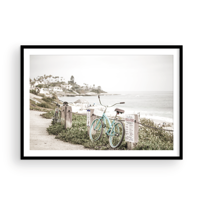 Fine art of horizontal landscape print by Southern California photographer Kim Dybczak of Salt Creek Prints, the image shows a light blue pastel beach cruiser leaning against a wooden post and chain fence. Another bicycle is visible behind it. The beach is in the background with people and a beach hut, located in Windansea Beach in La Jolla, California. Photograph in framed minimalist mock up