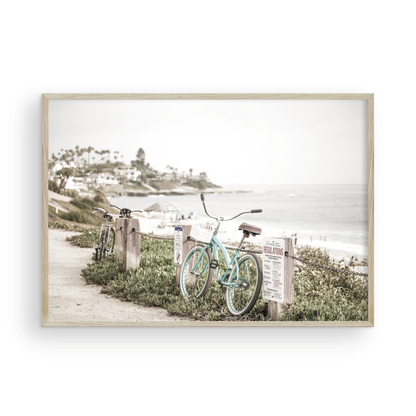 Fine art of horizontal landscape print by Southern California photographer Kim Dybczak of Salt Creek Prints, the image shows a light blue pastel beach cruiser leaning against a wooden post and chain fence. Another bicycle is visible behind it. The beach is in the background with people and a beach hut, located in Windansea Beach in La Jolla, California. Photograph in framed minimalist mock up