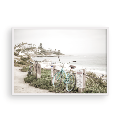 Fine art of horizontal landscape print by Southern California photographer Kim Dybczak of Salt Creek Prints, the image shows a light blue pastel beach cruiser leaning against a wooden post and chain fence. Another bicycle is visible behind it. The beach is in the background with people and a beach hut, located in Windansea Beach in La Jolla, California. Photograph in framed minimalist mock up