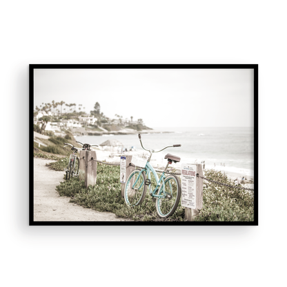 Fine art of horizontal landscape print by Southern California photographer Kim Dybczak of Salt Creek Prints, the image shows a light blue pastel beach cruiser leaning against a wooden post and chain fence. Another bicycle is visible behind it. The beach is in the background with people and a beach hut, located in Windansea Beach in La Jolla, California. Photograph in framed minimalist mock up