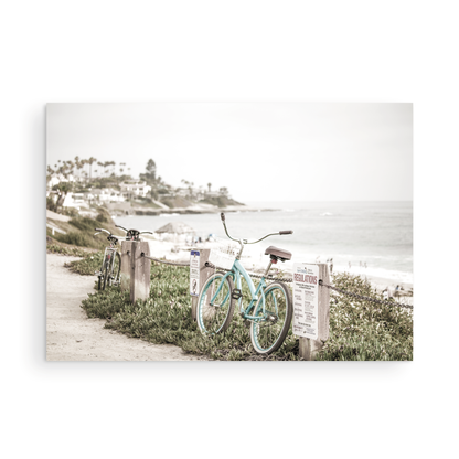 Fine art of horizontal landscape print by Southern California photographer Kim Dybczak of Salt Creek Prints, the image shows a light blue pastel beach cruiser leaning against a wooden post and chain fence. Another bicycle is visible behind it. The beach is in the background with people and a beach hut, located in Windansea Beach in La Jolla, California. Photograph in framed minimalist mock up