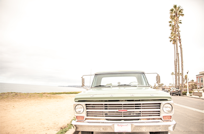 Nostalgic Southern California beach art featuring a classic light green Ford F-Series pickup truck parked by the San Diego coast. This horizontal surf print captures the vintage vehicle with a backdrop of iconic tall palm trees, a hazy beach, and the ocean, embodying surf vibes and perfect for coastal farmhouse decor.