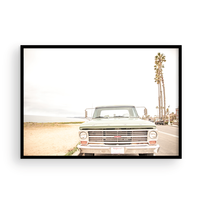 Nostalgic Southern California beach art featuring a classic light green Ford F-Series pickup truck parked by the San Diego coast. This horizontal surf print captures the vintage vehicle with a backdrop of iconic tall palm trees, a hazy beach, and the ocean, embodying surf vibes and perfect for coastal farmhouse decor. Photograph in minimalist framed mock up.