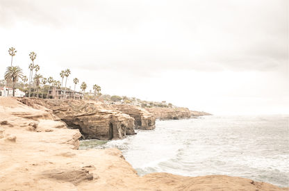 Fine art of Sunset Cliffs, San Diego California horizontal print of hazy high-angle landscape beach photography captures a light blue ocean meeting tall tan, brown cliffs rise as iconic coastal scenery. 