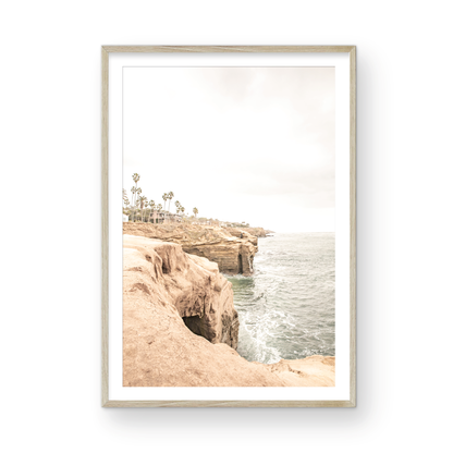 Fine art of Sunset Cliffs, San Diego California vertical print of hazy high-angle landscape beach photography captures a light blue ocean meeting tall tan, brown cliffs rise as iconic coastal scenery. Photograph in minimalist mock up.