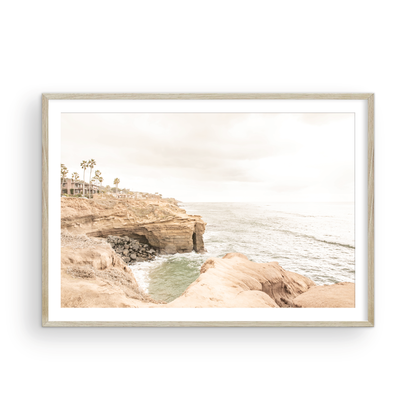 Fine art of Sunset Cliffs, San Diego California horizontal print of hazy high-angle landscape beach photography captures a light blue ocean meeting tall tan, rocky, brown cliffs rise as iconic coastal scenery. Photograph in minimalist mock up.
