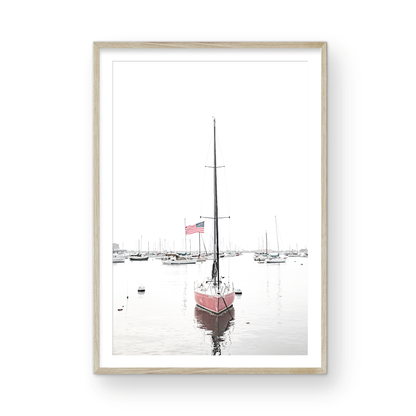 A vertical San Diego print featuring a lone red sailboat with an American flag, anchored in a calm San Diego harbor. This minimalist ocean print captures the essence of coastal photography and is perfect for modern coastal decor. Photograph in minimalist mock up.