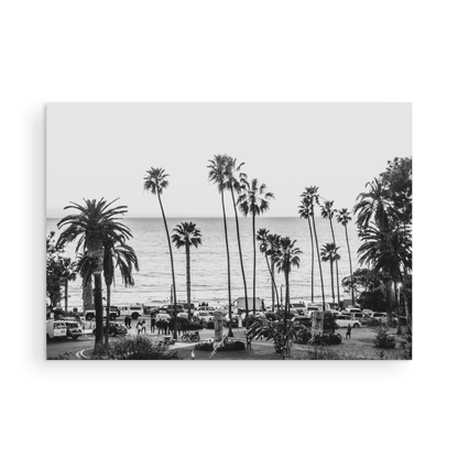 A classic black and white horizontal print of Swamis, the iconic San Diego surf spot, showcasing a panoramic view from above. This piece of Southern California travel photography features dozens of silhouetted palm trees against a bright sky, with a lively beach scene of cars and people below, stretching towards the ocean. Perfect as timeless beach art or neutral coastal decor for a surf vibe. Photograph in minimalist unframed mock up.