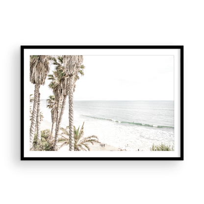Dreamy coastal palm tree print featuring several tall palm trees with shaggy trunks, and surfers walking down the tranquil beach. This vertical tropical print is captured at Swamis Beach on the Southern California coast, is bathed in bright, hazy sunlight, creating a pastel beach art effect. Evokes serene summer vibes, perfect for beach house decor. Photograph in minimalist surf art mock up.