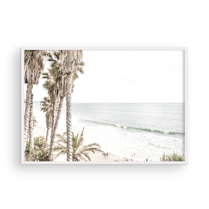 Dreamy coastal palm tree print featuring several tall palm trees with shaggy trunks, and surfers walking down the tranquil beach. This vertical tropical print is captured at Swamis Beach on the Southern California coast, is bathed in bright, hazy sunlight, creating a pastel beach art effect. Evokes serene summer vibes, perfect for beach house decor. Photograph in minimalist surf art mock up.