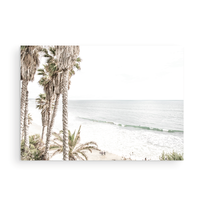 Dreamy coastal palm tree print featuring several tall palm trees with shaggy trunks, and surfers walking down the tranquil beach. This vertical tropical print is captured at Swamis Beach on the Southern California coast, is bathed in bright, hazy sunlight, creating a pastel beach art effect. Evokes serene summer vibes, perfect for beach house decor. Photograph in minimalist mock up.