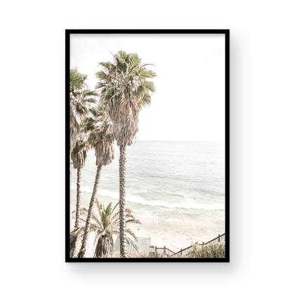 Dreamy coastal palm tree print featuring several tall palm trees with shaggy trunks, next to a staircase down to a tranquil beach. This vertical tropical print is captured at Swamis Beach on the Southern California coast, is bathed in bright, hazy sunlight, creating a pastel beach art effect. Evokes serene summer vibes, perfect for beach house decor. Photograph in minimalist surf art mock up.