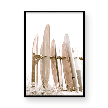 Neutral surfboard wall art. framed fine art beach photography for the modern coastal home. Minimalist vertical surf art print showcasing a line-up of surfboards in various lengths and soft, neutral pastel hues, resting on a simple wooden rack with some dry grass in the foreground. This piece of surf wall decor features a bright, hazy white backdrop, enhancing its clean aesthetic. Perfect as pastel surf decor or for adding surf vibes to kids surf room decor or a beach house. 