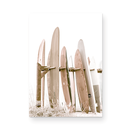 Neutral surfboard wall art. fine art photography for beach house decor. Minimalist vertical surf art print showcasing a line-up of surfboards in various lengths and soft, neutral pastel hues, resting on a simple wooden rack with some dry grass in the foreground. This piece of surf wall decor features a bright, hazy white backdrop, enhancing its clean aesthetic. Perfect as pastel surf decor or for adding surf vibes to kids surf room decor or a beach house. 