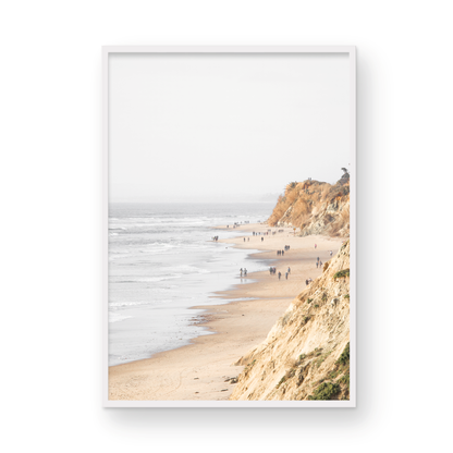 Fine art of Torrey Pines, San Diego California vertical print of hazy high-angle landscape beach photography captures a light blue ocean meeting a sandy beach with many beach goers. To the right, tall tan and brown cliffs rise as iconic coastal scenery. Photograph in minimalist framed mock up.