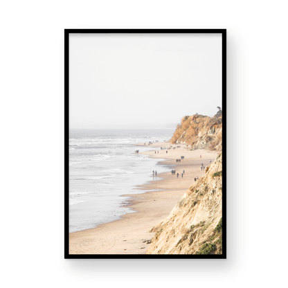 Fine art of Torrey Pines, San Diego California vertical print of hazy high-angle landscape beach photography captures a light blue ocean meeting a sandy beach with many beach goers. To the right, tall tan and brown cliffs rise as iconic coastal scenery. Photograph in minimalist framed mock up.