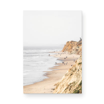 Fine art of Torrey Pines, San Diego California vertical print of hazy high-angle landscape beach photography captures a light blue ocean meeting a sandy beach with many beach goers. To the right, tall tan and brown cliffs rise as iconic coastal scenery. Photograph in minimalist unframed mock up.
