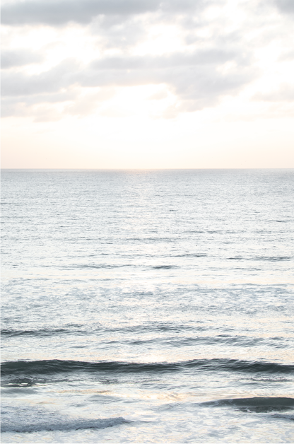 Fine art of vertical landscape print by Southern California photographer Kim Dybczak of Salt Creek Prints, featuring a bright image capturing pale blue ocean waves, light gray clouds in a bright sky. Gentle, small waves in the near and far distance. The sky is a uniform, pale white, creating a soft, overcast atmosphere. 