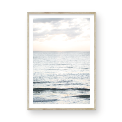 Fine art of vertical landscape print by Southern California photographer Kim Dybczak of Salt Creek Prints, featuring a bright image capturing pale blue ocean waves, light gray clouds in a bright sky. Gentle, small waves in the near and far distance. The sky is a uniform, pale white, creating a soft, overcast atmosphere. Photograph in framed minimalist mock up
