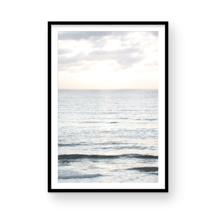 Fine art of vertical landscape print by Southern California photographer Kim Dybczak of Salt Creek Prints, featuring a bright image capturing pale blue ocean waves, light gray clouds in a bright sky. Gentle, small waves in the near and far distance. The sky is a uniform, pale white, creating a soft, overcast atmosphere. Photograph in framed minimalist mock up